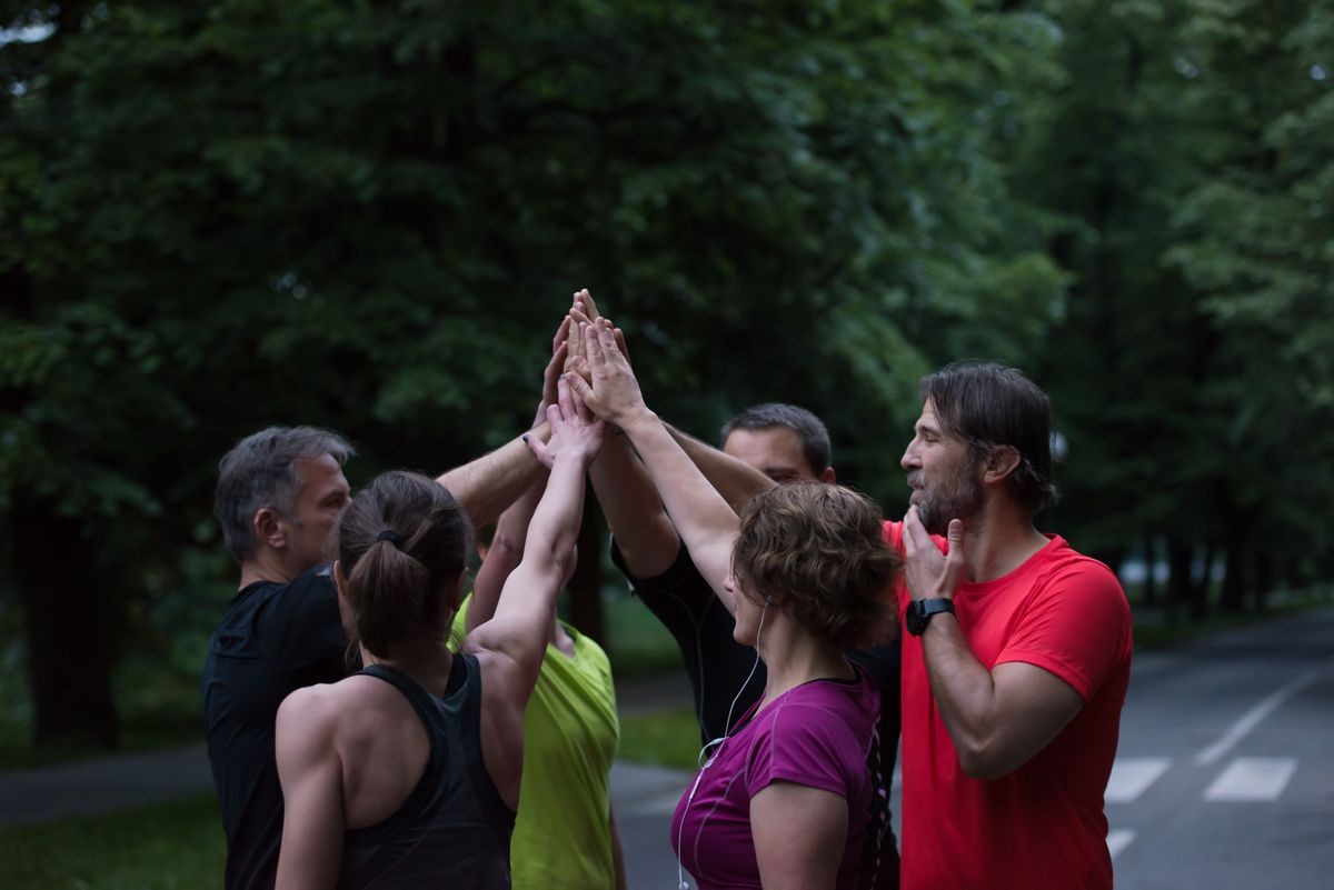 Group of healthy runners giving high five to each other while celebrating success after a training session.